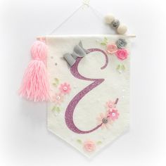 the number three is decorated with pink flowers and tassels on a white banner