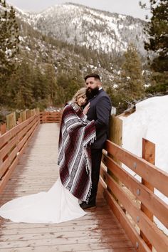 a bride and groom standing on a bridge in the snow