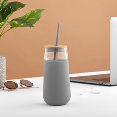 a gray tumbler with a straw in front of a laptop on a white table