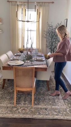 a woman standing in front of a dining room table set with place settings on it