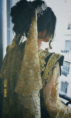 a woman wearing a gold and black dress with a tiara on her head looking out the window