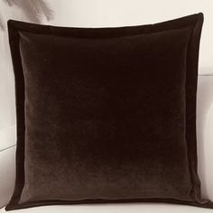 a black velvet pillow sitting on top of a white couch next to a feathery wallpaper