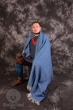 a man is sitting on a chair wrapped in a blue blanket and holding a hat