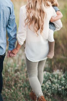 a man and woman holding hands while walking through a field