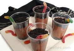 four cups filled with dirt and candy on top of a white tray next to a black bag