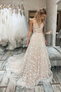 a woman in a wedding dress looking down at her gown hanging on the rack with other dresses behind her