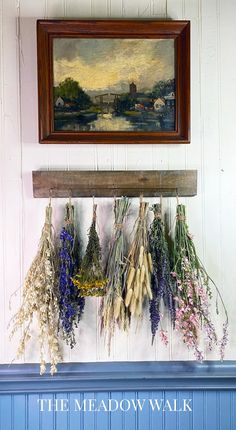 a painting hanging on the wall above a blue mantle filled with dried flowers and herbs