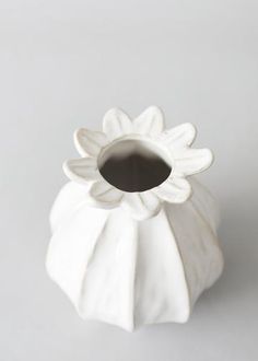 a white flower vase sitting on top of a gray tableclothed surface with a black spot in the center