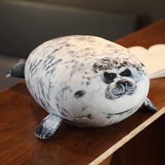 a stuffed seal is sitting on top of a wooden table next to a book and pen