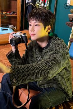 a young man sitting on top of a bed holding a camera