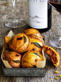 several pastries in a box next to a bottle of wine and some glasses on a table