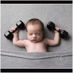 a baby is holding two black dumbbells on his head while laying down in a gray blanket