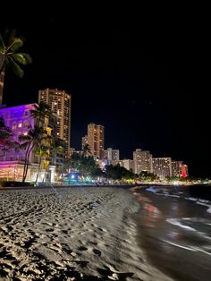 the beach is lit up at night with palm trees and buildings in the back ground