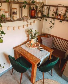 a dining room table with two green chairs next to it and hanging plants on the wall