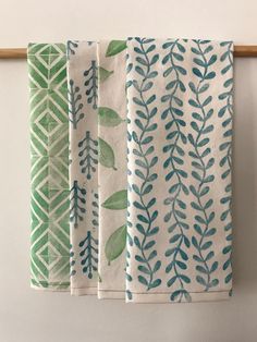 three tea towels hanging on a clothes line with green leaves painted on the front and back