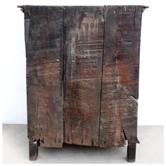 an old wooden cabinet with two legs and some paint on the top, sitting in front of a white wall