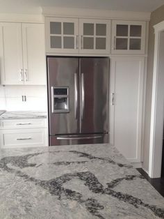 an empty kitchen with marble counter tops and white cupboards on either side of the refrigerator