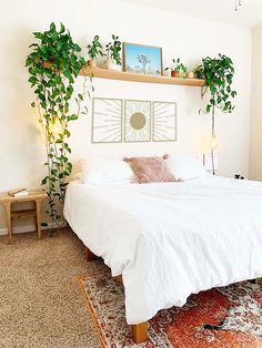 a white bed sitting in a bedroom next to a wooden shelf filled with potted plants