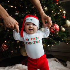 a baby wearing a santa hat standing in front of a christmas tree