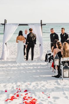 a bride and groom are getting married on the beach with red rose petals in front of them