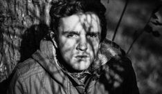 a black and white photo of a man leaning against a tree with his head turned to the side