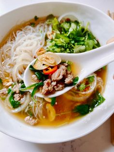 a white bowl filled with soup and veggies next to chopsticks on a table