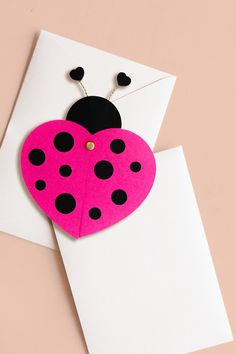 a pink and black heart shaped card with a ladybug on the front, attached to a white envelope