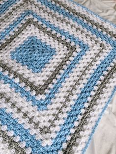 a crocheted blanket on a bed with white and blue squares in the middle