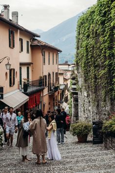 people are walking down the cobblestone street in an old town with tall buildings