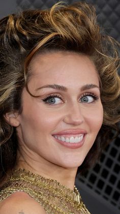 a close up of a woman with blonde hair and blue eyes wearing a gold dress