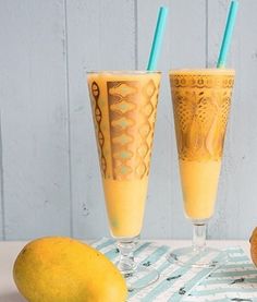 two glasses filled with orange juice next to an orange on a striped table cloth and some lemons