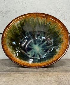 a brown and green bowl sitting on top of a wooden table next to a white wall