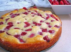 a cheesecake with strawberries on top sits next to a bowl of raspberries