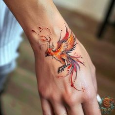 a woman's hand with a bird tattoo on her left wrist and red watercolor paint splatters all over it