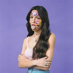 a woman with face paint on her body and arms crossed in front of a purple background