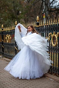 a woman in a white dress is posing by a fence