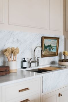 a kitchen with white cabinets and marble counter tops, gold pulls on the faucet