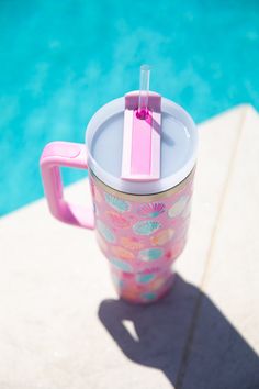 a pink and white cup sitting next to a swimming pool with a straw in it