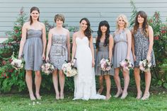 a group of women standing next to each other in front of some flowers and bushes