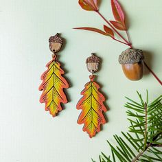 two wooden earrings with acorns and leaves hanging from them on a white surface