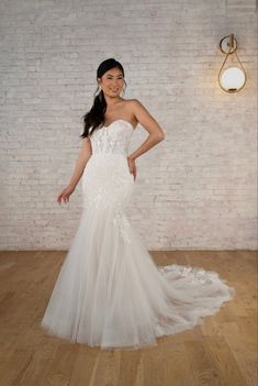 a woman in a white wedding dress standing on a wooden floor next to a brick wall