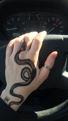 a woman's hand on the steering wheel of a car with a snake tattoo