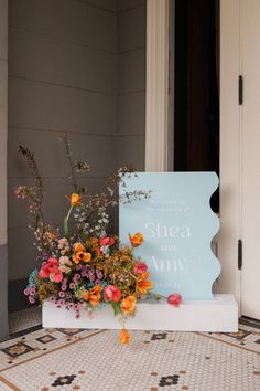 an arrangement of flowers sits on the floor next to a sign that reads, sheea and ann