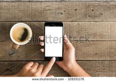 a person holding a smart phone with a white screen next to a cup of coffee