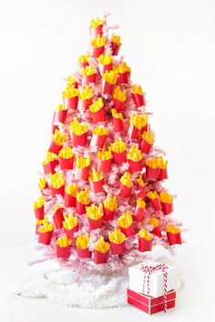 a red and yellow christmas tree with presents on it's bottom, in front of a white background