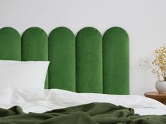 a bed with green headboard and pillows on top of it next to a plant