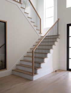 a white staircase with wooden handrails next to a mirror on the wall in a room