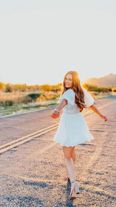 a girl in a white dress is walking down the road with her arms spread out