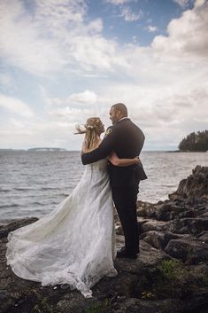 a bride and groom standing on rocks by the water