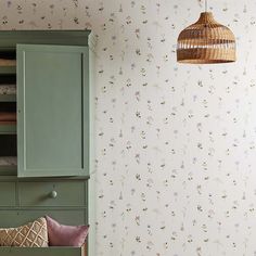 a green cabinet sitting next to a wall covered in floral wallpaper and a basket hanging from the ceiling